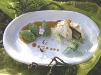 Ein weißer Teller mit grünen Nockerln und einer Blätterteigtasche. Soße ist tröpfchenweise auf dem Teller verteilt.